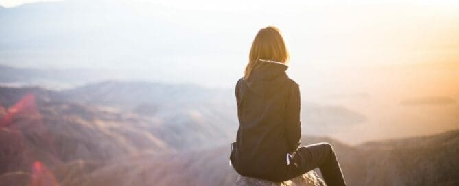 girl sitting on mountain top observing the view