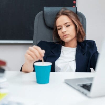 woman sitting in office drained out, stirring coffee cup