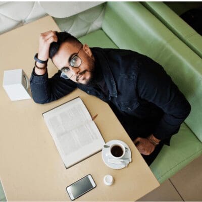 man-wearing glasses sitting in cafe reading book having coffee looking up